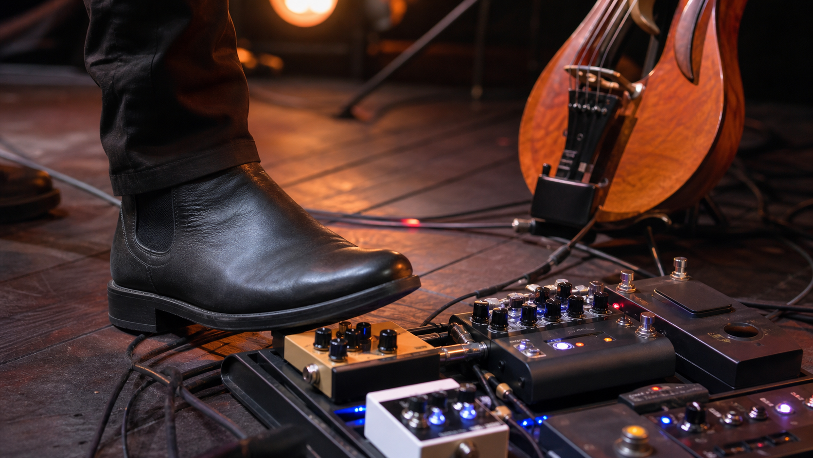 Близък кадър на ботуш върху компактен amp sim педал в electric violin pedalboard под топли концертни светлини