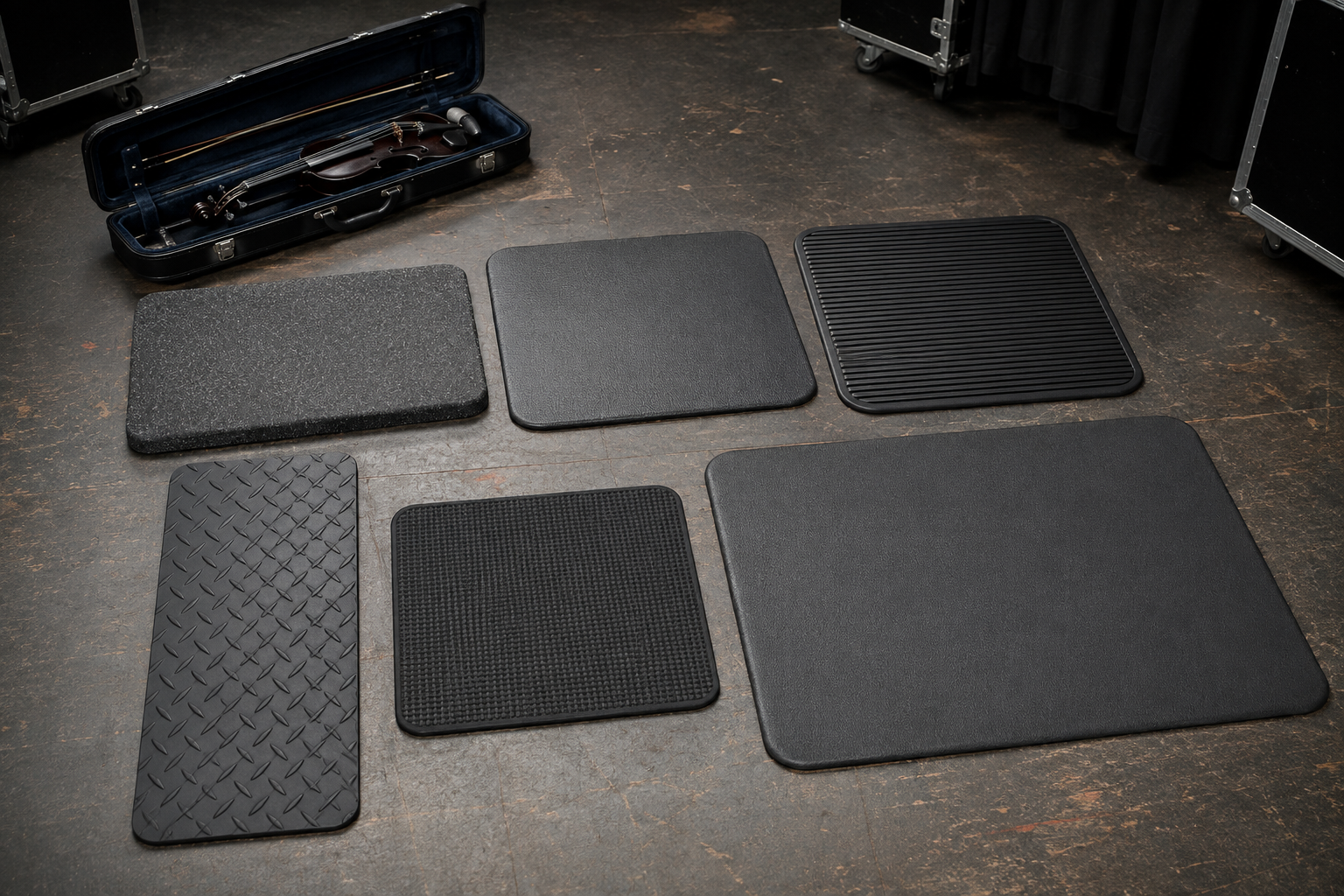 Six black and charcoal anti-fatigue mats compared beside an electric violin case backstage