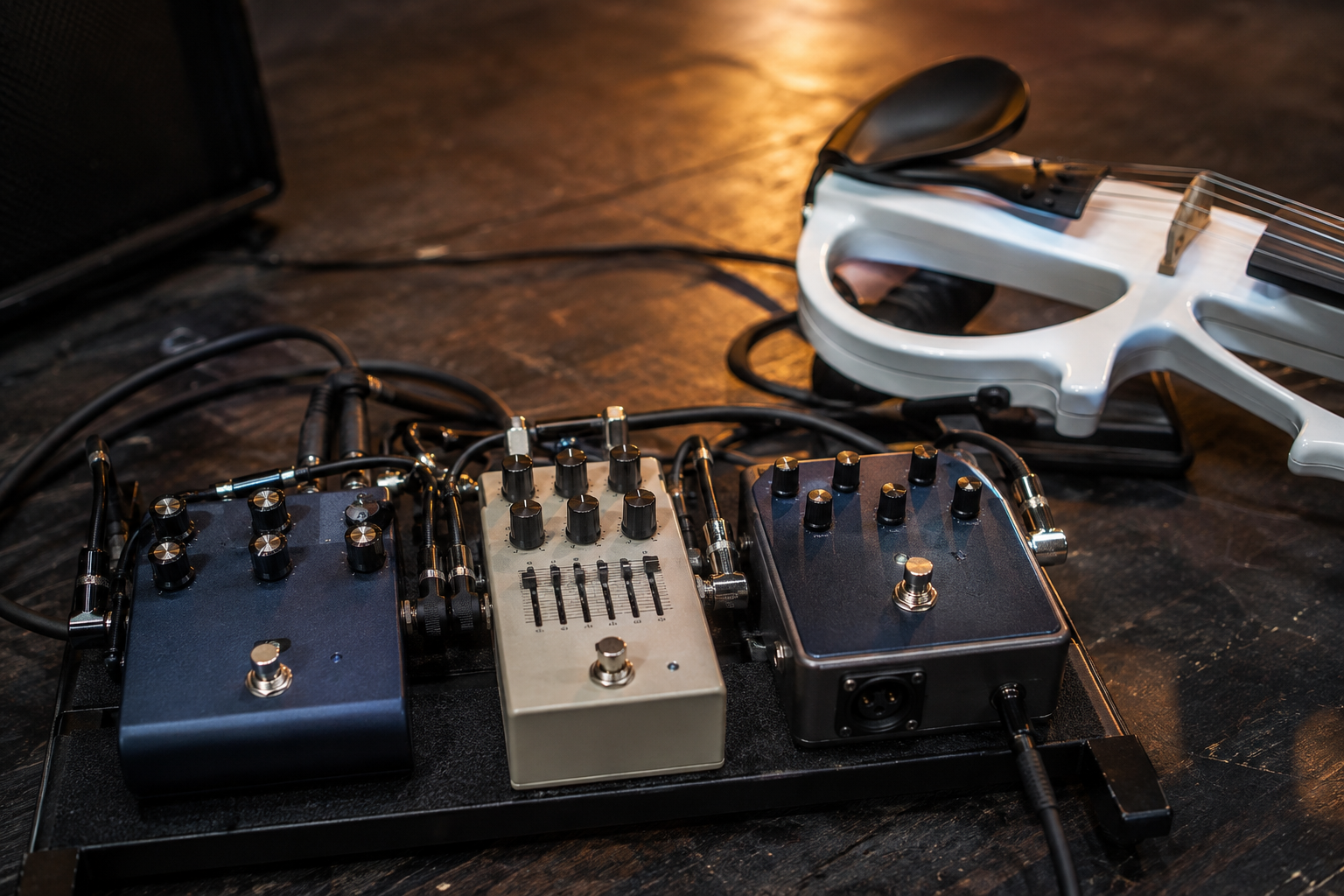 Close-up of an electric violin pedalboard during soundcheck with chorus, EQ, and DI pedals under warm backstage light