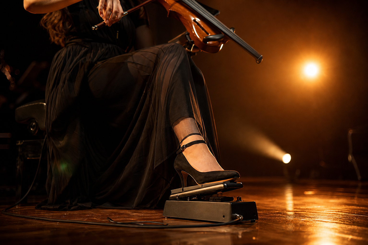 Close concert shot of an electric violinist shaping phrasing with a foot on an expression pedal during a live swell