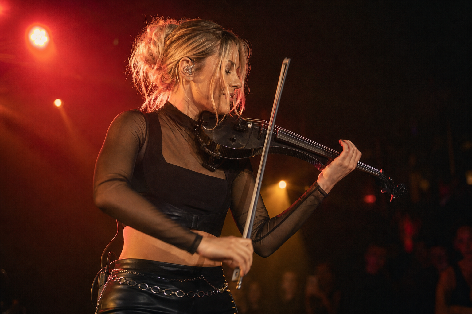 Electric violinist performing under red stage lights while wearing clear in-ear monitors during a club show