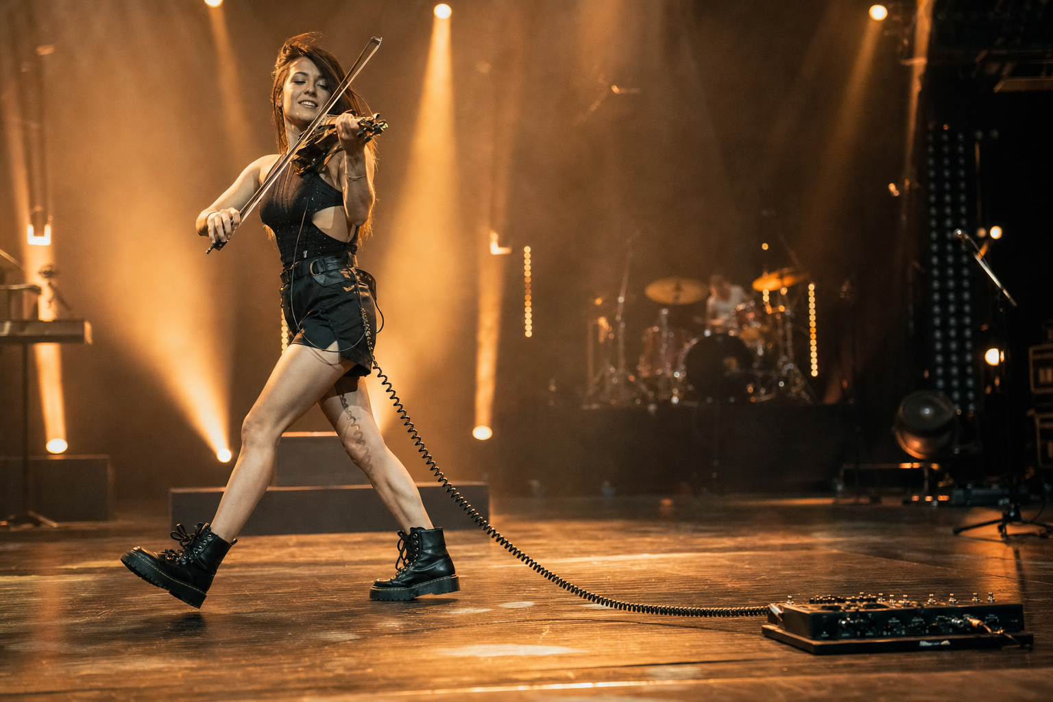 Electric violin performer walking across stage with a coiled instrument cable extending toward a pedalboard
