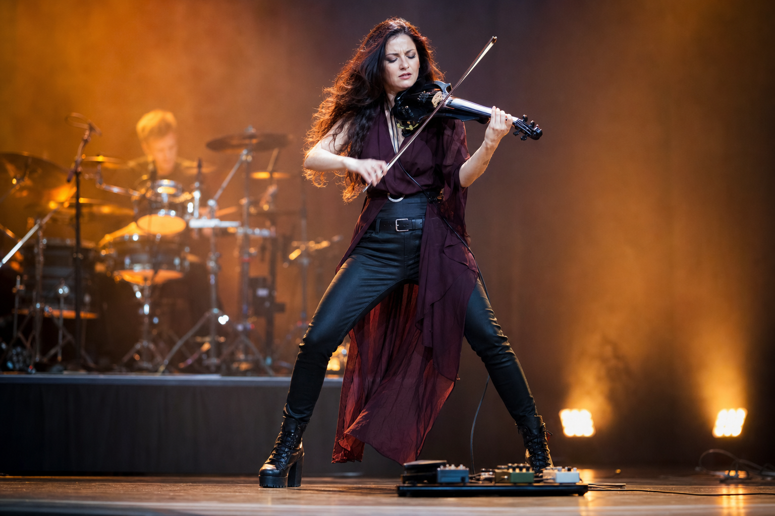 Electric violin performer in a dramatic live moment playing with a saturated lead tone above a small pedalboard under amber stage lights