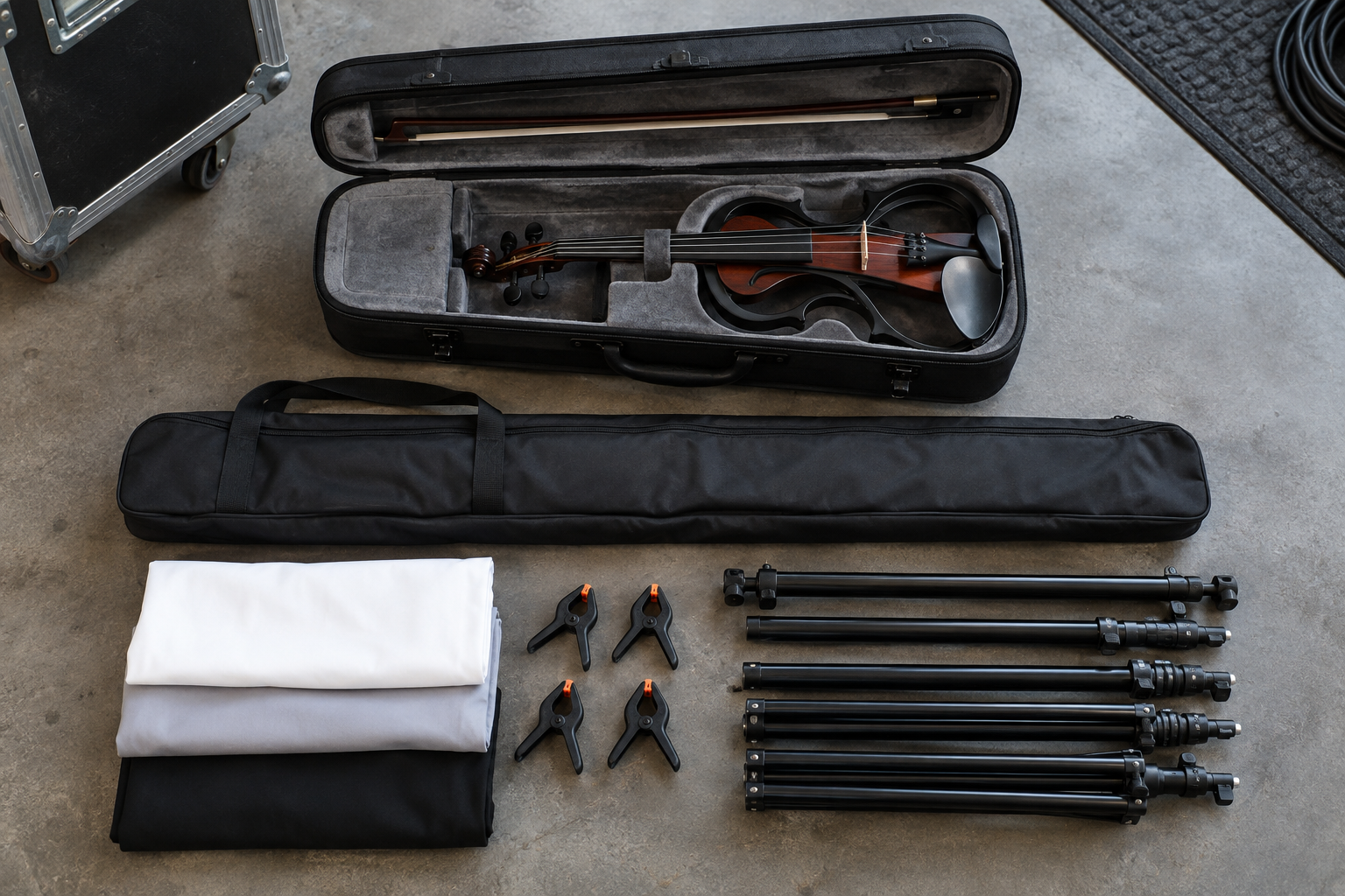 Folded portable backdrop kit and carry bag beside an electric violin performance case